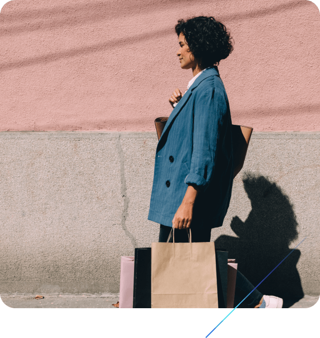 woman walking in a sunny urban context, holding several bags from retail purchases