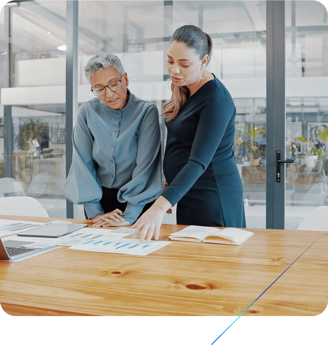 Two women in an office meeting room discussing printed graphs.