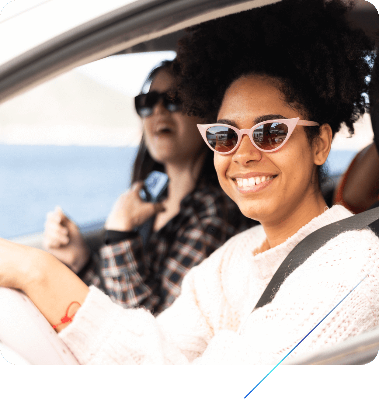 Two smiling women driving a car along the ocean