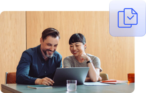 Two people smiling while discussing information on a laptop in an office meeting room